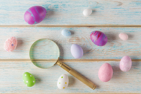 Top view of a magnifying glass  next to colorful, textured eggs on a rustic wooden surface. Easter eggs hunting and searchの写真素材