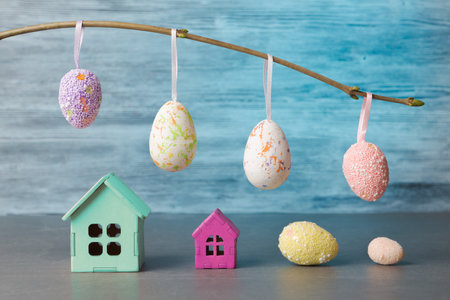 An Easter-themed display featuring vibrant eggs hanging from a branch and small pastel-colored...