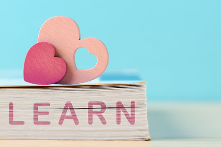 A heartwarming educational concept with a stack of books and heart cutouts, symbolizing a passion for learning against blue background with copy spaceの写真素材
