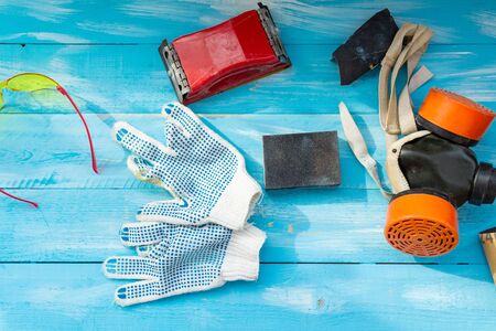 Abrasives, sanding paper, sponges and wheel, respirator on the blue wooden background close up