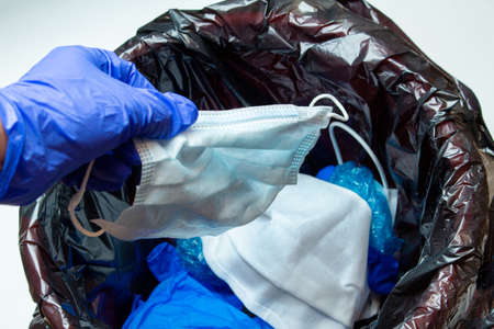 Hand in medical gloves throwing out discarded, used protective masks in the trash bin after quarantineの写真素材