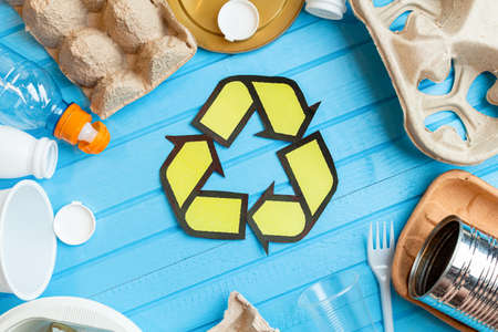 color plastic, metal cans, paper, cardboard waste with recycling sign on blue background