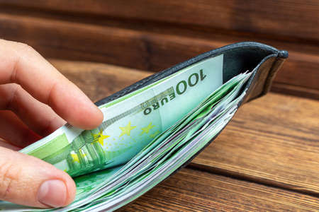hands holding wallet full of money banknotes on wooden background
