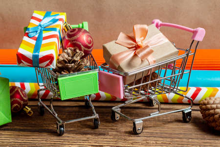 Gift boxes in shopping cart and colorful wrapping paper on a wooden brown background. The concept of preparing for the holidays New Year and Christmas.