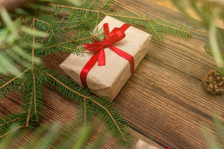 Fur spruce pine coniferous branches, gift box craft paper with red bow on the brown brushed wooden backgroundの写真素材