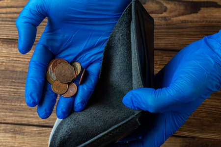 empty blue wallet in hands in medical gloves holding coins after financial economic crisisの写真素材