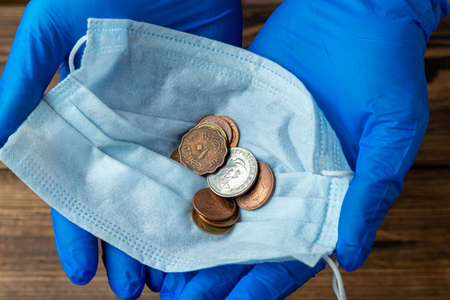 protective mask with coins in hands in medical gloves after financial economic crisisの写真素材