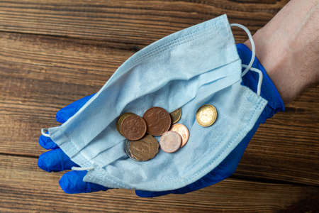 protective mask with coins in hands in medical gloves after financial economic crisisの写真素材