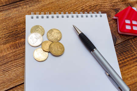 Red home house notepad pen on the banknotes and coins background euro pile pack real estate concept expenses property buying mockup copy space close up background selective focusの写真素材