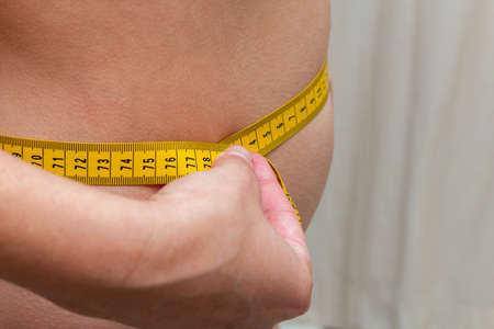 woman measures the waist with a yellow tape. Diet fitness concept.の写真素材