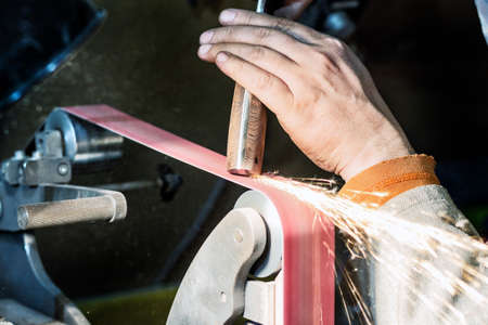 Blade sharpening creating on a belt grinder process. Knife making master hands close up.