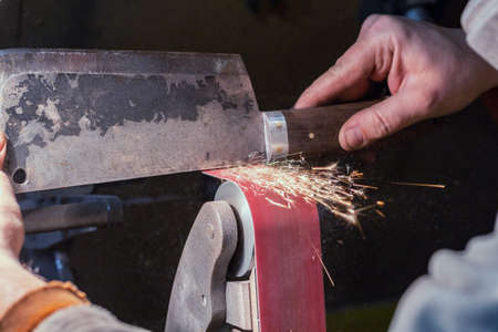 Blade sharpening creating on a belt grinder process. Knife making master hands close up.