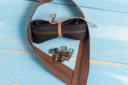Black and brown metal brass zippers stripes with sliders for handmade leatherwork leathercraft on the blue wooden backgroundの写真素材