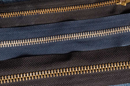 Pack a lot of black navy metal brass zippers stripes with sliders pattern for handmade sewing tailoring leatherwork leathercraft on the blue wooden backgroundの写真素材