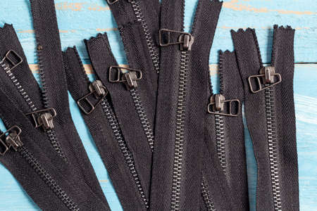 Pack a lot of black metal antique zippers stripes with sliders pattern for handmade sewing tailoring haberdashery leather craft on the blue denim backgroundの写真素材