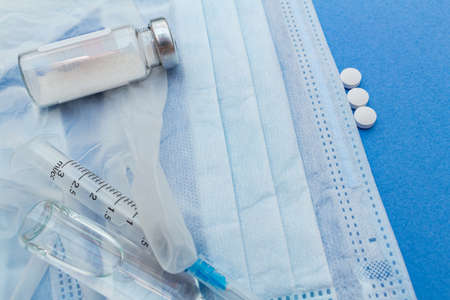 medical protective masks with syringe, ampoule, medicine bottle, pills on a blue background.