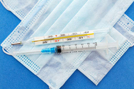 medical protective masks with thermometer, syringe on a blue background.