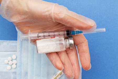 syringe and medicine bottle in the hand on the blue medical protective mask background