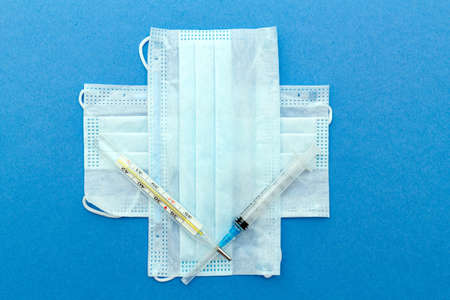 medical protective masks cross shape with thermometer, syringe on a blue background with copy space.