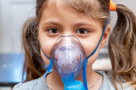 Little girl doing inhalation procedure at home using a mask