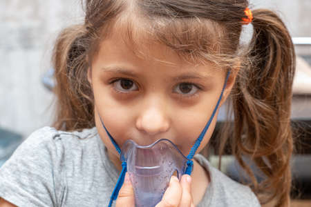 Little girl doing inhalation procedure at home using a maskの写真素材