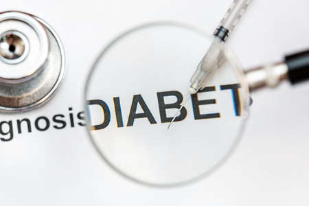 Words diabetes diagnosis with syringe through magnifying glass.の写真素材
