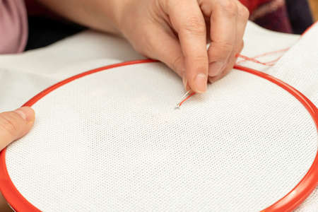 process of cross stitching embroidery on fabric in a frame with handsの写真素材