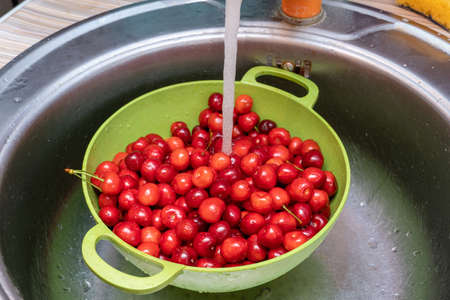 Washing red sweet cherries under the tap in a green bowl, colander close upの写真素材