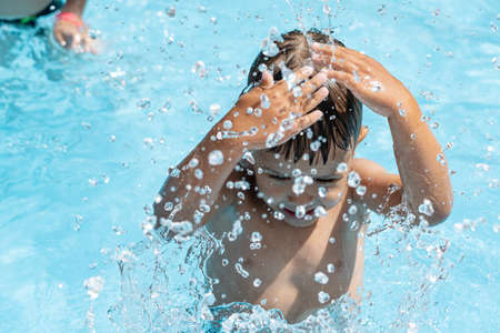 Little child swims in the pool, plays splashing water