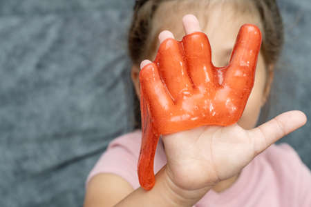 Child playing with red color slime, gunge, gel in handsの写真素材