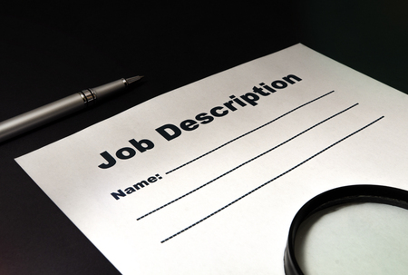 Job description with magnifying glass and pen on black background close-up.