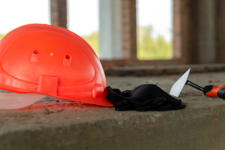A pair of gloves and a Mason's helmet at the construction site of a red brick house.の写真素材