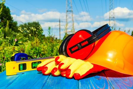 Protective helmet, headphones, gloves on a wooden table, against the background of nature and high voltage posts.. Construction site safety.の写真素材