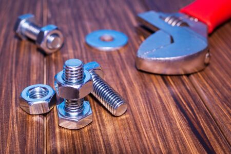 Metal bolt and nut on brown vintage wooden background with adjustable wrenchの写真素材