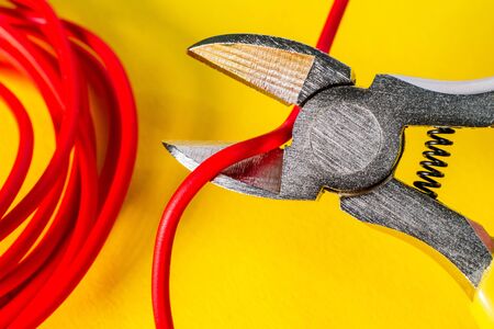 Pliers tool cutting red electric wire closeup on a yellow backgroundの写真素材