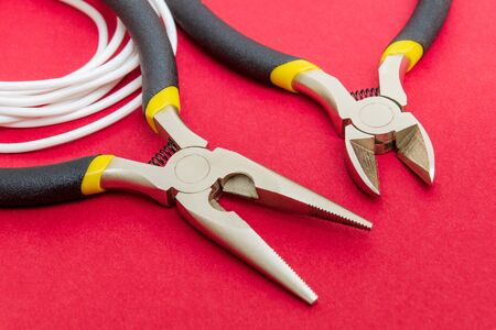Pliers tool and wires for electrician closeup, service and repairing concept on red background