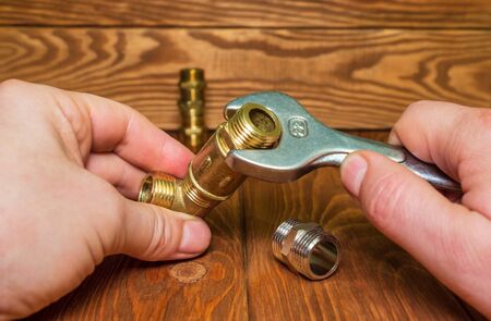 Worker connects plumbing fittings making repairs with a wrench on vintage wooden tableの写真素材