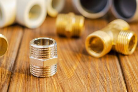 Brass fitting against the background of spare parts for plumbing on wooden vintage boards