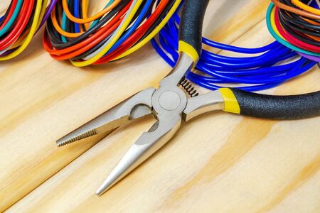 Pliers tool and wires for electrician closeup service repairing concept on wooden boards close up