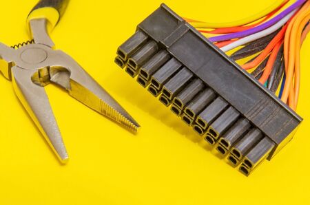 Pliers for a master electrician and wires with contacts of different colors on yellow background