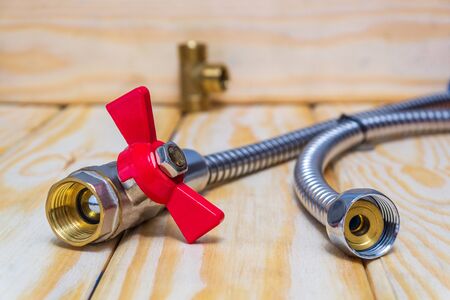 Metal ball valve with a red handle with fittings and hose prepared for repair on wooden boards