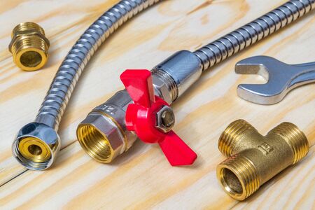 Metal ball valve with a red handle with fittings and hose prepared for repair on wooden boardsの写真素材