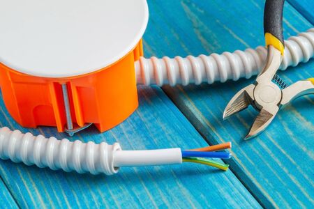Junction box with wire and tools for repairing electrics in house on blue wooden boards