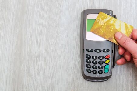 Hand applies bank card to money terminal for payment on office desk, top view