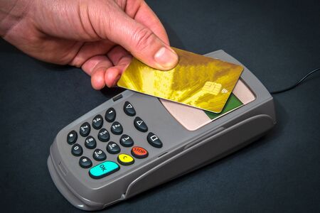 Hand applies bank card to money terminal for payment on black office desk top view