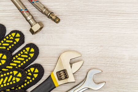 Plumbing equipment repair tools adjustable wrench, hoses, gloves, flexible connection on bright wooden surfaceの写真素材