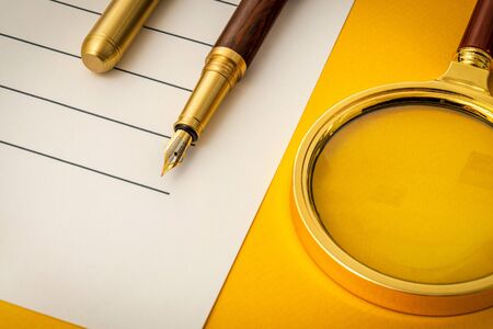 Beautiful office still life on a yellow table with pen and magnifying glass preparing for recordingsの写真素材