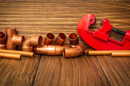 Red pipe cutter and copper pipes with connectors on vintage wooden boardsの写真素材