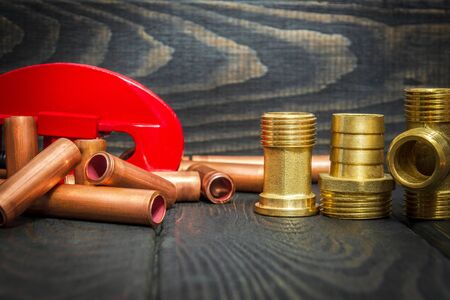 Red pipe cutter and copper pipes, brass fittings with connectors for plumbing repairs on black...