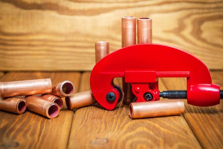 Red pipe cutter and copper pipes with connectors for plumbing repairs on vintage wooden boards close upの写真素材